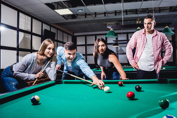 Fototapeta premium Group of young cheerful friends playing billiards.