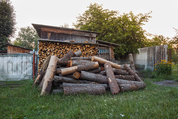 Cut logs lie randomly in the back yard. Stack of logs. Preparation of firewood for the winter. 