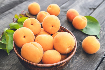 Delicious ripe apricots in a bowl next to green leaves on a wooden table.