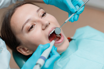 Fototapeta premium Patient in dental chair. Dentist's hands with blue gloves work with a dental tools. Beautiful young woman having dental treatment at dentist's office.