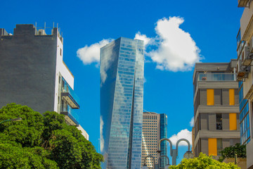 Obraz na płótnie Canvas perfect city street landmark wallpaper photography of Tel Aviv Israeli capital with common small living building foreground and glass skyscraper tower on vivid blue sky with white cloud background 