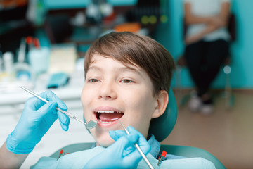 Little boy with open mouth examining dental inspection at dentist office. Dentist's hands with blue gloves work with a dental tools. Healthy teeth concept.