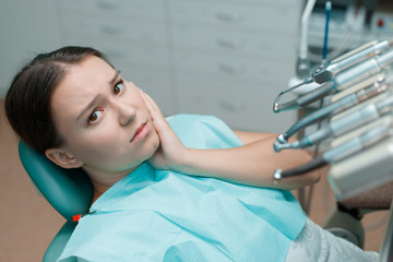 Patient in dental chair. Beautiful young woman having dental treatment at dentist's office. Girl touch her cheek suffering from painful toothache.