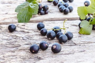 Black currant lies next to the green leaves on a wooden background. Juicy natural fruits currant.