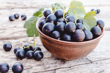 Fresh ripe currant berries in a bowl on wooden background near green leaves. Juicy fruits currants. Black currant