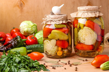 Assorted pickled vegetables in jars: cucumbers, tomatoes, cabbage, zucchini and peppers with garlic, dill and bay leaves in jars on a wooden background, horizontal photo