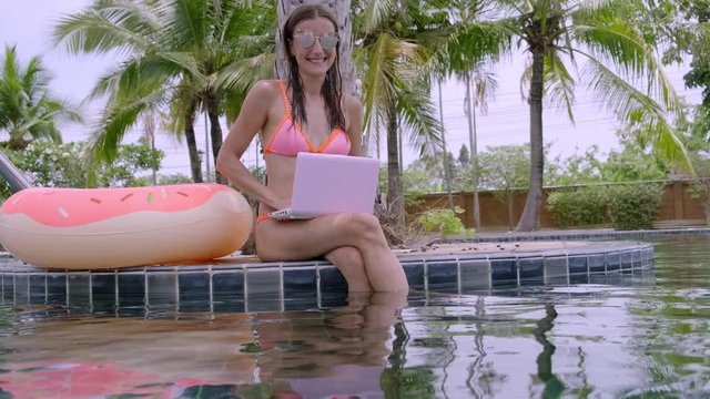 A young woman sits by the pool with minicomputer. selective focus