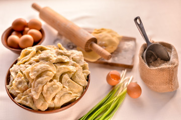 ready-made dumplings Ukrainian national dish in a clay dish on a board with ingredients eggs, flour and greens