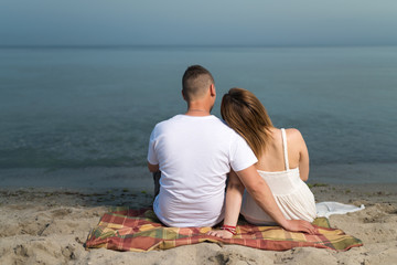 Romantic portrait of couple in love hugs sitting on the beach at the sunset. Against the backdrop of the sea.