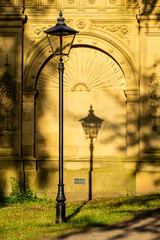 The evening sun casts a shadow of an old-fashioned lamp post on to the carved wall of Titus Salt's mausoleum in Saltaire