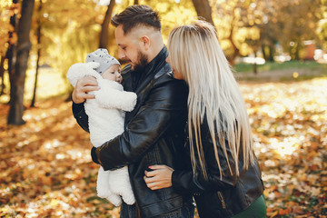 Family in a autumn park. Woman in a black jacket. Cute newborn little girl with parents