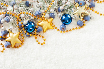 Fototapeta premium Christmas corner composition with green fir branch, gold garland, stars, blue glass baubles and berries on white snow background