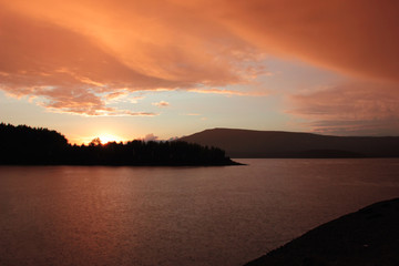 orange and pink clouds at sunset over a mountain lake