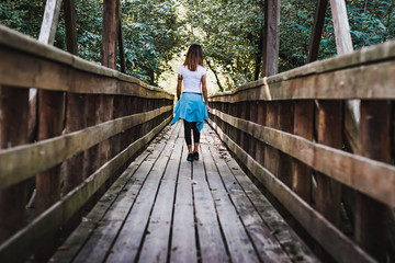 Fototapeta na wymiar A girl walking on a wooden pier in the middle of nature