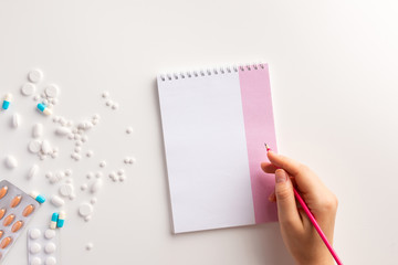 Femаle hand, notepad, pencil, drugs on white background. Flat lay.