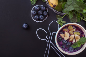 Fototapeta na wymiar Bowl of smoothies with berries on a chalkboard with spoons