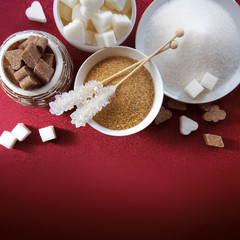 Various types and shapes of sugar on red background with empty space for logo or title. Top view. Sugar hearts, clubs diamonds, spades. Stick sugar, cane brown white sugar.