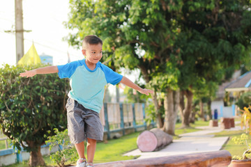 Portrait image of 5 years and 2 months old. Kid and exercise for health concept. Happy Asian child boy warm up his body before he run and exercise. He walking on a wooden bar at the playground.