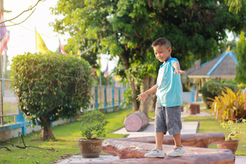 Portrait image of 5 years and 2 months old. Kid and exercise for health concept. Happy Asian child boy warm up his body before he run and exercise. He walking on a wooden bar at the playground.