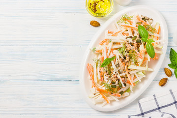 Turnip carrot apple salad with yogurt dressing, nuts, seeds on wooden background. Top view, space for text
