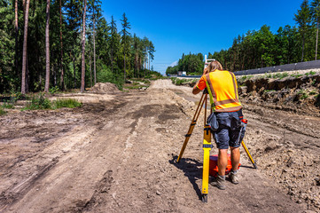 Surveyor engineer (worker) with equipment (theodolite or total positioning station) on the construction site of the road or highway