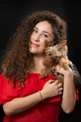 Young latin lady holding her Yorkshire Terrier dog for a portrait. She is smiling to the camera.