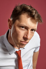 Portrait of a young brunet man posing in a studio against a red background.