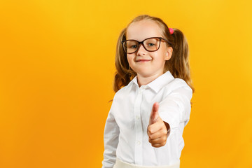 Portrait of a cute attractive little girl. The child shows thumb up on a yellow background.