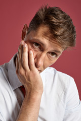 Portrait of a young brunet man posing in a studio against a red background.