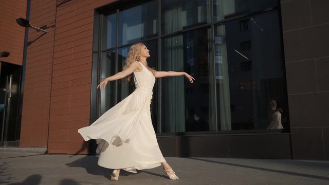 carefree girl in a flowing dress dancing and spinning on tiptoes against the background of modern buildings