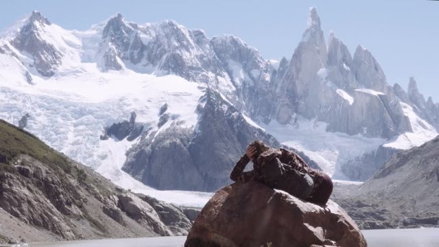 Female mountaineer resting over a rock in front of the majestic Patagonian mountain range. Lake torre in the national park Los Glaciares. 4k