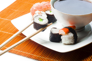 Sushi held in chopsticks over a bowl with sauce on a white background