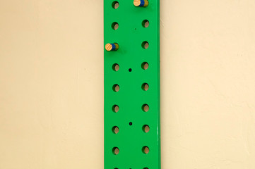 A green painted exercise peg board on wall with wooden pegs and copy space.