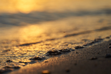 Closeup of water bubble from the waves on the sandy coast at sunset. Golden hour background. Copy spase