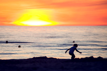 A silhouette of a child on the beach on sunset. Children, summer and holiday concept