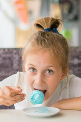 Little girl eating blue ice cream in a cafe. Girl delighted with ice cream. Adorable little girl eating ice cream at summer. vertical photo