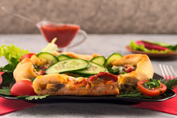 Slices of pizza with mushrooms and cheese on a black plate. Slices of fresh vegetables - cucumbers, tomatoes with dill. Spicy tomato sauce. Quick delicious dinner.
