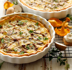 Mushroom quiche with addition chanterelle mushrooms and brown mushrooms on a wooden table, close up