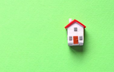 Dream about own house concept with miniature toy house with red roof on a green background.