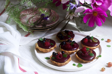 Shortbread tartlets with berry custard and flowers on a light background.