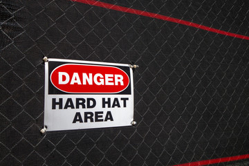 red white black danger hard hat area sign on net covered fence