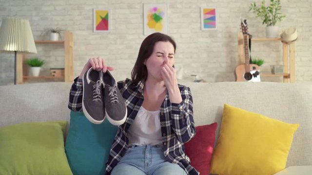 Young woman holding shoes in her hands and smell unpleasant