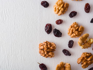 A variety of peeled walnuts and raisins on a white wooden background. View from above. Plenty of...