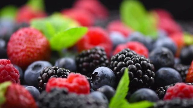Berries. Various colorful berries background. Strawberry, raspberry, blackberry, blueberry closeup over black. Healthy eating. Rotation. Slow motion 4K UHD video footage. 3840X2160