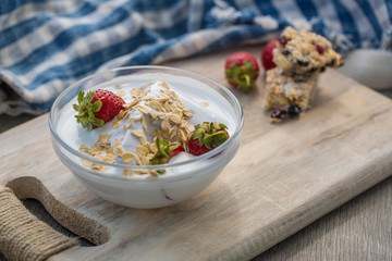 Bowl of fresh strawberries and yogurt. Photo of breakfast bowl with farm fresh strawberries and granola served on a wooden board.