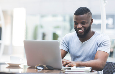 Smiling african man textmessaging on laptop in cafe
