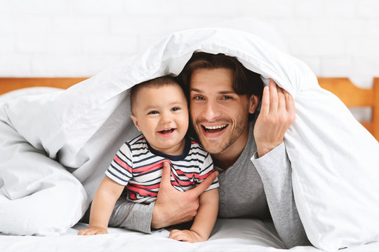 Caucasian Man Hiding With Baby Under Blanket In Bed