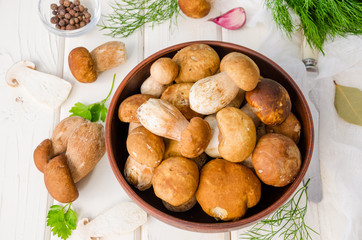 Fresh forest white mushrooms in a bowl with spices and fresh herbs on a wooden background