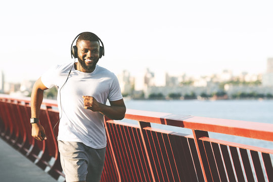 Cheerful Black Man Running Along The Bridge, Listening To Music