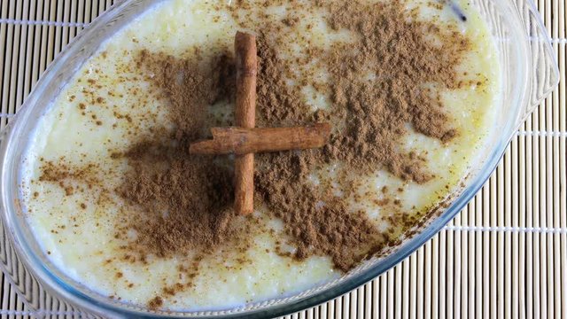 rice pudding with cinnamon on wooden table, accompanied by wooden spoon and cinnamon splinters, top view